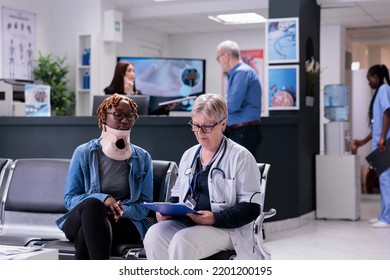 Senior Medic Consulting Woman At Facility, Wearing Cervical Neck Collar To Cure Injury And Pain. Specialist And Patient With Medical Foam Brace Talking About Recovery In Waiting Room At Health Center.