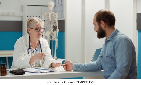 Senior medic and sick patient attending health checkup visit in cabinet, receiving prescription paper to buy treatment and medication after appointment. Disease report at consultation. - Powered by Shutterstock