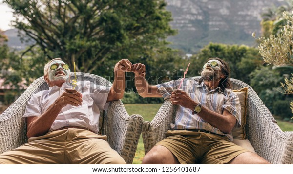 Senior men\
with clay facial mask on face giving each other fist bump. Elderly\
men enjoying facial spa\
treatment.