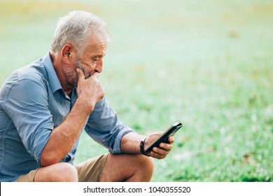 Senior men using a smartphone while sitting on grass in the park - Powered by Shutterstock