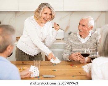 Senior men and women play card game poker during friendly gatherings at home. Couple enthusiastically participate in game, believe in luck, collect chips, distribute winnings - Powered by Shutterstock