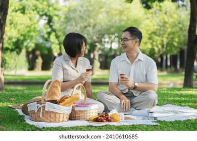 Senior middle aged couple happily embracing and drinking together during a picnic in the park outdoors - Powered by Shutterstock