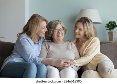 Senior mom and young adult daughter visiting elder senior grandmother, resting on sofa at home, chatting, talking, holding hands, hugging with love, care, enjoying family weekend - Powered by Shutterstock