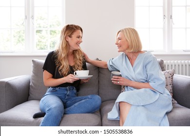 Senior Mother With Adult Daughter Sitting On Sofa Indoors Drinking Coffee And Talking