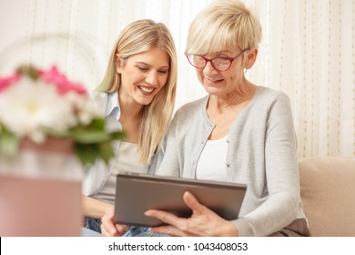 Senior Mother And Daughter Browsing The Internet On A Tablet. Happy Family Moments At Home.