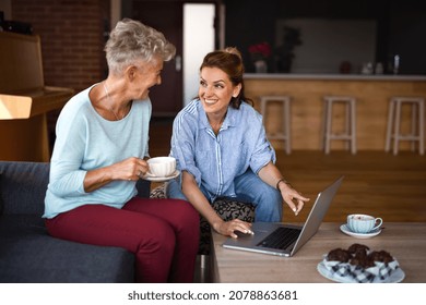 Senior Mother Having Coffee With Adult Daughter Indoors At Home, Sitting, Talking And Using Tablet.