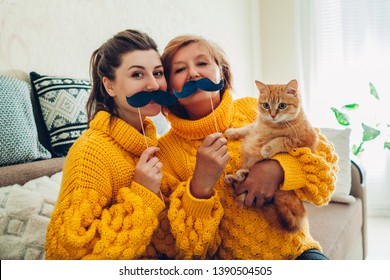 Senior Mother And Her Adult Daughter Taking Selfie With Cat Using Photo Booth Props At Home. Mother's Day Concept.