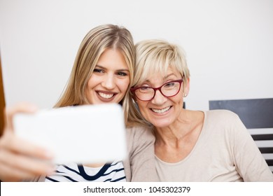 Senior mother and her daughter smiling and posing for a selfie while sitting by dinner table in bright room. Daughter holding phone. Happy family moments at home. - Powered by Shutterstock