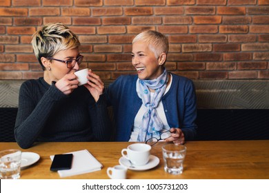 Senior Mother Sitting In Cafe Bar Or Restaurant With Her Middle Age Daughter And Enjoying In Conversation.