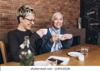 Senior Mother Sitting In Cafe Bar Or Restaurant With Her Middle Age Daughter And Enjoying In Conversation.