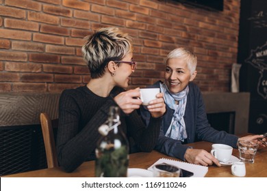 Senior Mother Sitting In Cafe Bar Or Restaurant With Her Middle Age Daughter And Enjoying In Conversation.