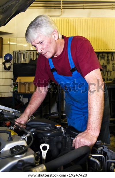 A\
senior motor mechanic servicing a car inside a\
garage