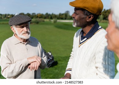 Senior Multiethnic Friends Looking At Man In Flat Cap On Golf Field