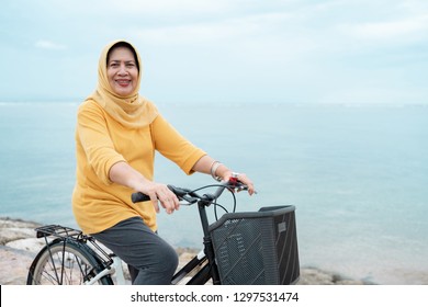 senior muslim woman with scarf riding a bike at the beach - Powered by Shutterstock