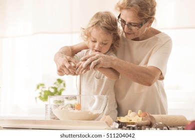 Senior nanny helping child to break the egg into a bowl
