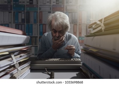 Senior Office Worker Using An Obsolete Keyboard, He Is Having Difficulties And Thinking With Hand On Chin