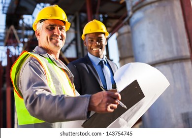 Senior Oil Industry Worker Holding Clipboard And Blueprint With Manager In Plant