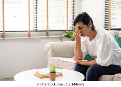 Senior old Asian woman feel stressed, headache sitting alone on sofa at home