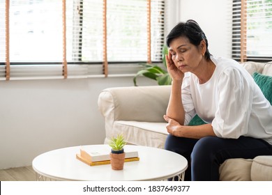 Senior old Asian woman feel stressed, headache sitting alone on sofa at home