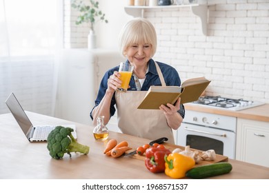 Senior old caucasian woman grandmother in apron cooking healthy vegetarian vegan food meal at home in kitchen, reading culinary book for new recipes, drinking fresh orange juice - Powered by Shutterstock