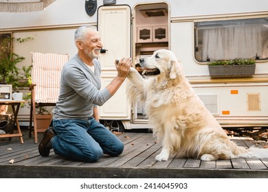 Senior old elderly man traveler pet owner walking a dog, golden retriever labrador, teaching him tricks together on the porch of trailer motor home camper van - Powered by Shutterstock