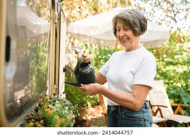 Senior old elderly woman grandmother watering her plants roses flowers outdoors outside in the garden of her house. Florist doing gardening. Pensioner`s hobby activity - Powered by Shutterstock