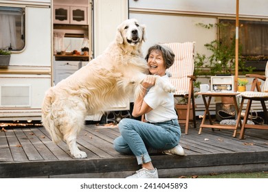 Senior old elderly woman traveler adventurer wife playing with her dog labrador domestic animal golden retriever on the porch of trailer camper van motor home - Powered by Shutterstock