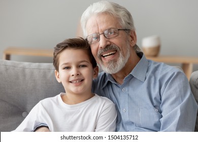 Senior Old Grandfather Embracing Little Child Grandson Happy Faces Looking At Camera, Grandkid Small Boy And Elder Grandpa Bonding Sit On Sofa, Close Up Portrait, Two Generation Men Family Concept