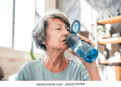 Senior old grandmother woman drinking water from bottle after training home workout yoga class. Rehydration concept. Thirsty athlete drinking water with electrolytes - Powered by Shutterstock