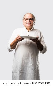 Senior Or Old Indian Asian Man Eating From Empty White Plate Or Bowl Using Spoon And Fork - Standing Isolated Over White Background With Different Expressions