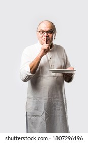 Senior Or Old Indian Asian Man Eating From Empty White Plate Or Bowl Using Spoon And Fork - Standing Isolated Over White Background With Different Expressions