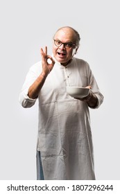 Senior Or Old Indian Asian Man Eating From Empty White Plate Or Bowl Using Spoon And Fork - Standing Isolated Over White Background With Different Expressions