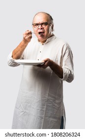 Senior Or Old Indian Asian Man Eating From Empty White Plate Or Bowl Using Spoon And Fork - Standing Isolated Over White Background With Different Expressions