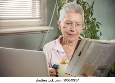 Senior Old Lady Reading A Magazine And Having Her Morning Cup Of Black Coffee