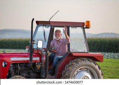 Senior old man driving small tractor in field and waving hand - Powered by Shutterstock