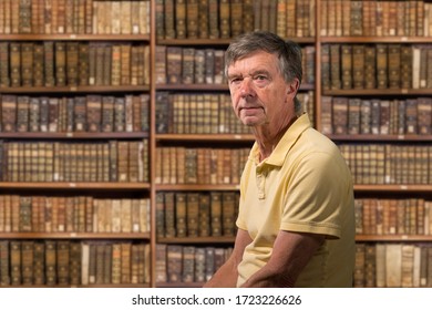 Senior Old Man Looking At Camera With A Background Of Shelves Of Old Books As If In Library Of A Stately Home