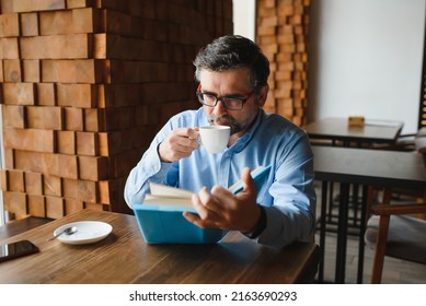 Senior Old Man Reading A Book In A Coffee Shop, Enjoying His Literary Hobby.