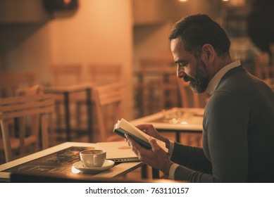 Senior Old Man Reading A Book In A Coffee Shop, Enjoying His Literary Hobby