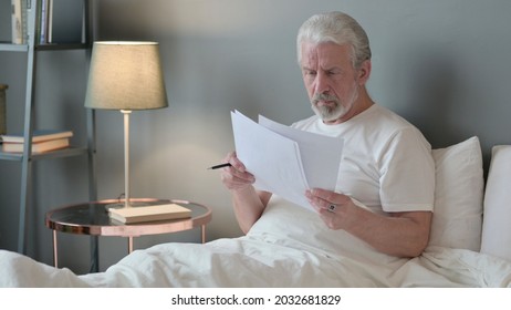 Senior Old Man Reading Documents In Bed