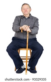 Senior Or Old Man Sitting Down On Old Wooden Chair With His Cane To Rest, Wearing Blue Corduroy And Slippers, Isolated On White.