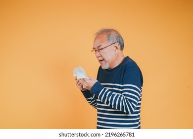 Senior Old Man Sneezing With Tissue, Asian Elderly Man Sick, Cold Having Fever And Flu Sinus From Sickness Virus Problem Use Tissue, Pensioner Unwell On The Yellow Background