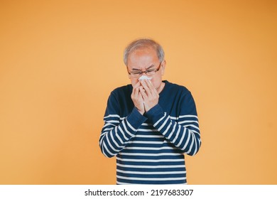 Senior Old Man Sneezing With Tissue, Asian Elderly Man Sick, Cold Having Fever And Flu Sinus From Sickness Virus Problem Use Tissue, Pensioner Unwell On The Yellow Background