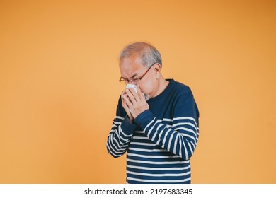 Senior Old Man Sneezing With Tissue, Asian Elderly Man Sick, Cold Having Fever And Flu Sinus From Sickness Virus Problem Use Tissue, Pensioner Unwell On The Yellow Background