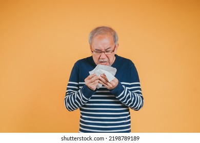 Senior Old Man Sneezing With Tissue, Asian Elderly Man Sick, Cold Having Fever And Flu Sinus From Sickness Virus Problem Use Tissue, Pensioner Unwell On The Yellow Background