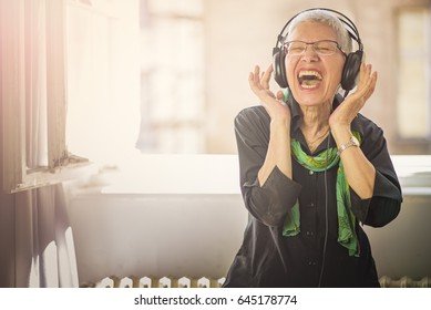 Senior old woman listening to her favourite music through big headphones, enjoying the rich sound - Powered by Shutterstock