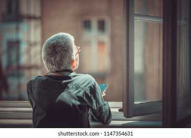 Senior Old Woman Looking Through A Window, Feeling Nostalgic And Melancholic