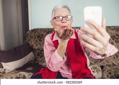 Senior old woman sending love and kisses to her family over skype or viber using her cellphone - Powered by Shutterstock