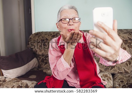 Senior old woman sending love and kisses to her family over skype or viber using her cellphone