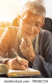 Senior Old Woman Writing Down Letters On A Piece Of Paper, Recording A Journal Or Diary Entry Or Writing A Novel