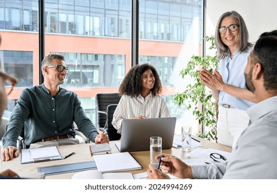 Senior older female executive ceo and happy multicultural business people discuss corporate project at boardroom table. Smiling diverse corporate team working together in modern meeting room office.